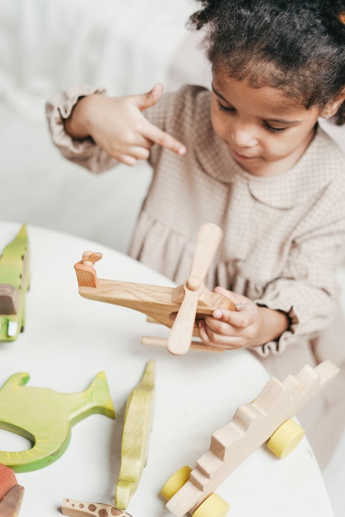 An adorable child plays with a wooden airplane toy indoors, surrounded by colorful wooden toys.