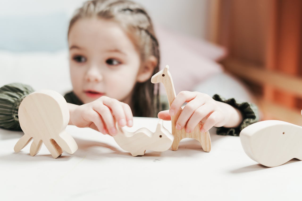 A young girl engaging in imaginative play with wooden animal toys in a bright indoor setting.