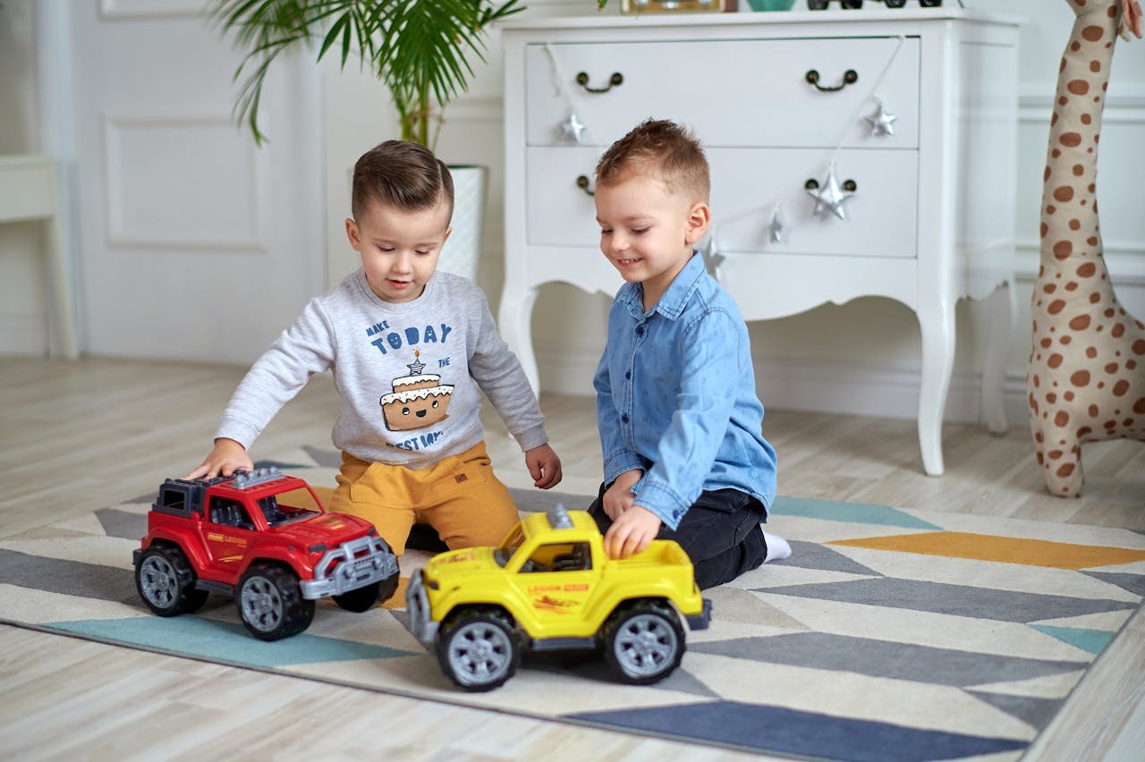 Menu Two young boys enjoy playing with toy cars in a bright, cozy room.