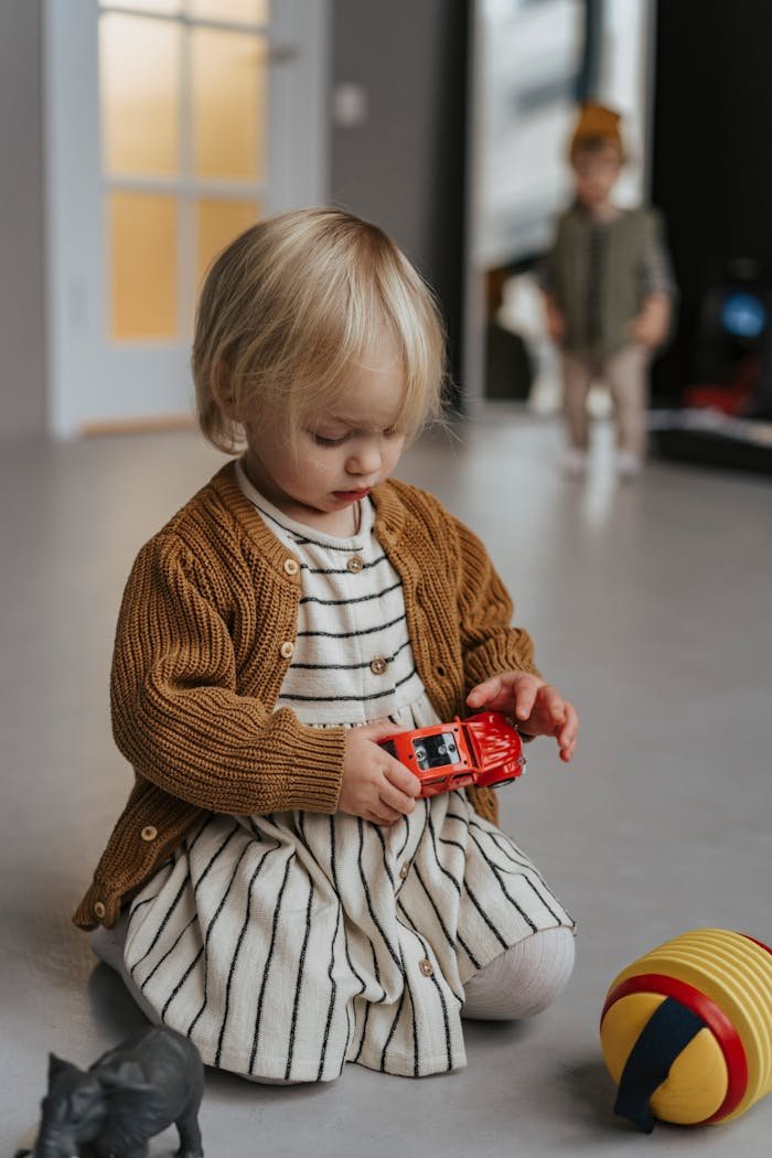 Cute toddler enjoying playtime indoors with a toy car and stuffed animal.